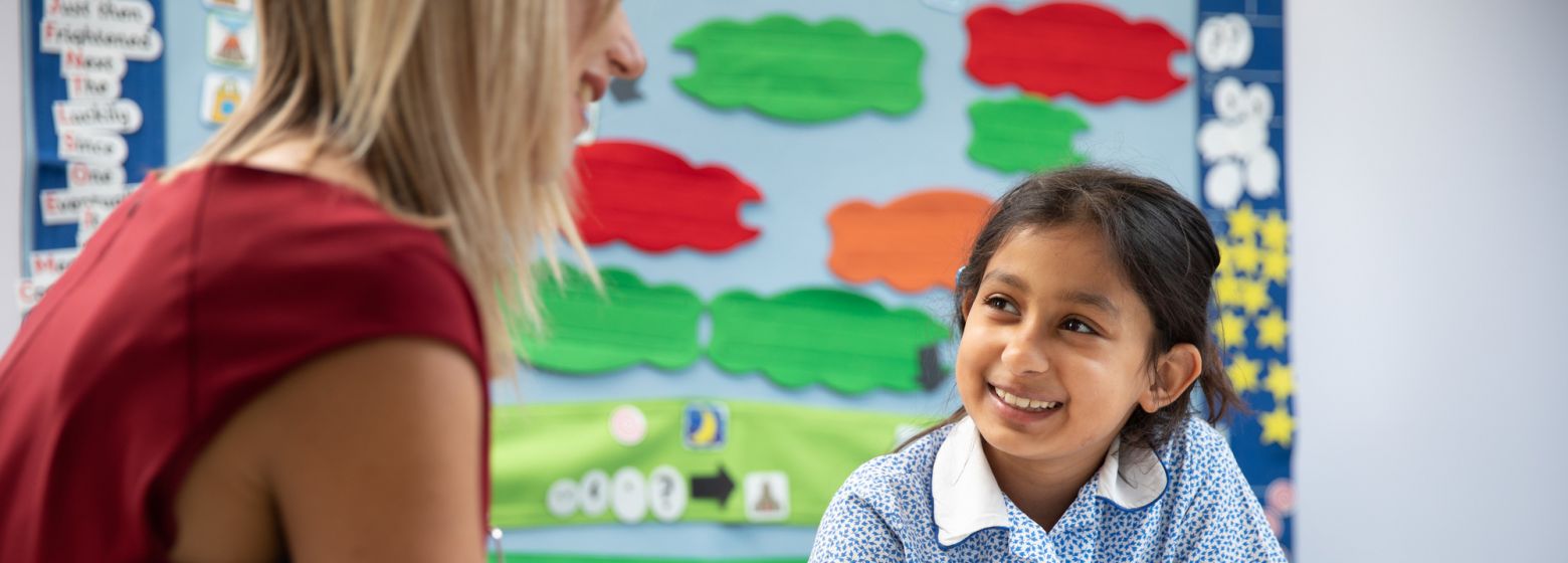 child writing with a pencil and smiling at a teacher