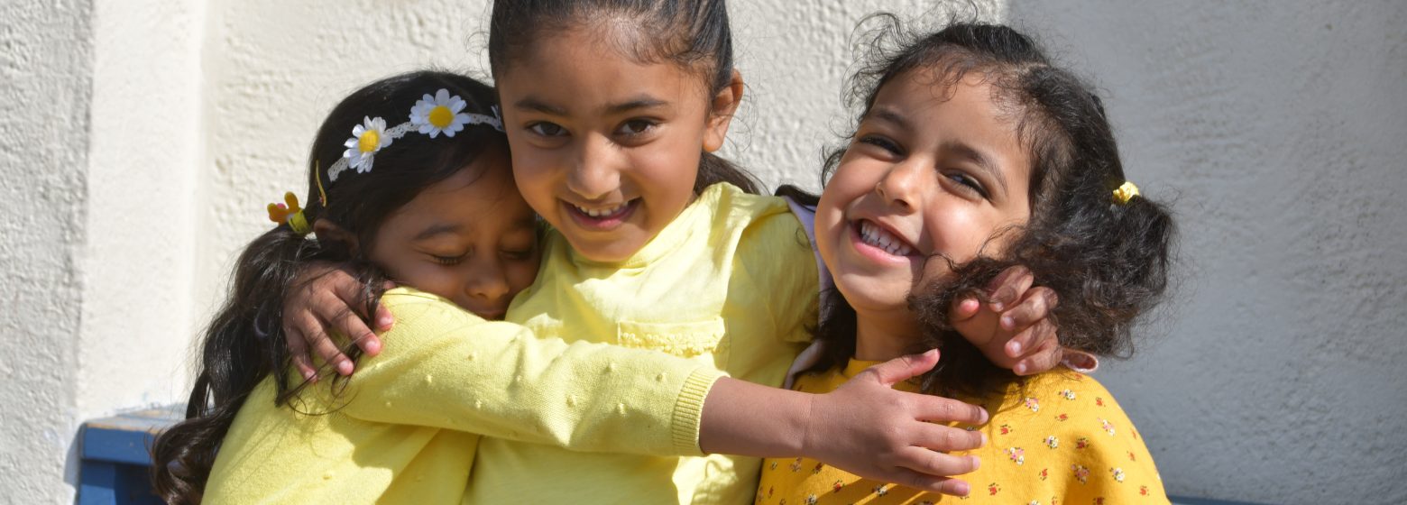 3 schoolgirls hugging each other, all wearing yellow tops