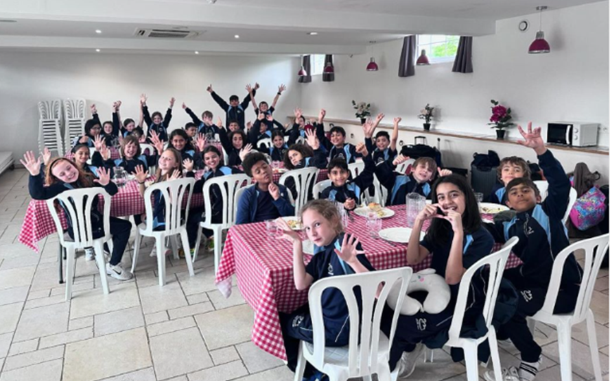 lots of school students sitting around tables and posing for a photo